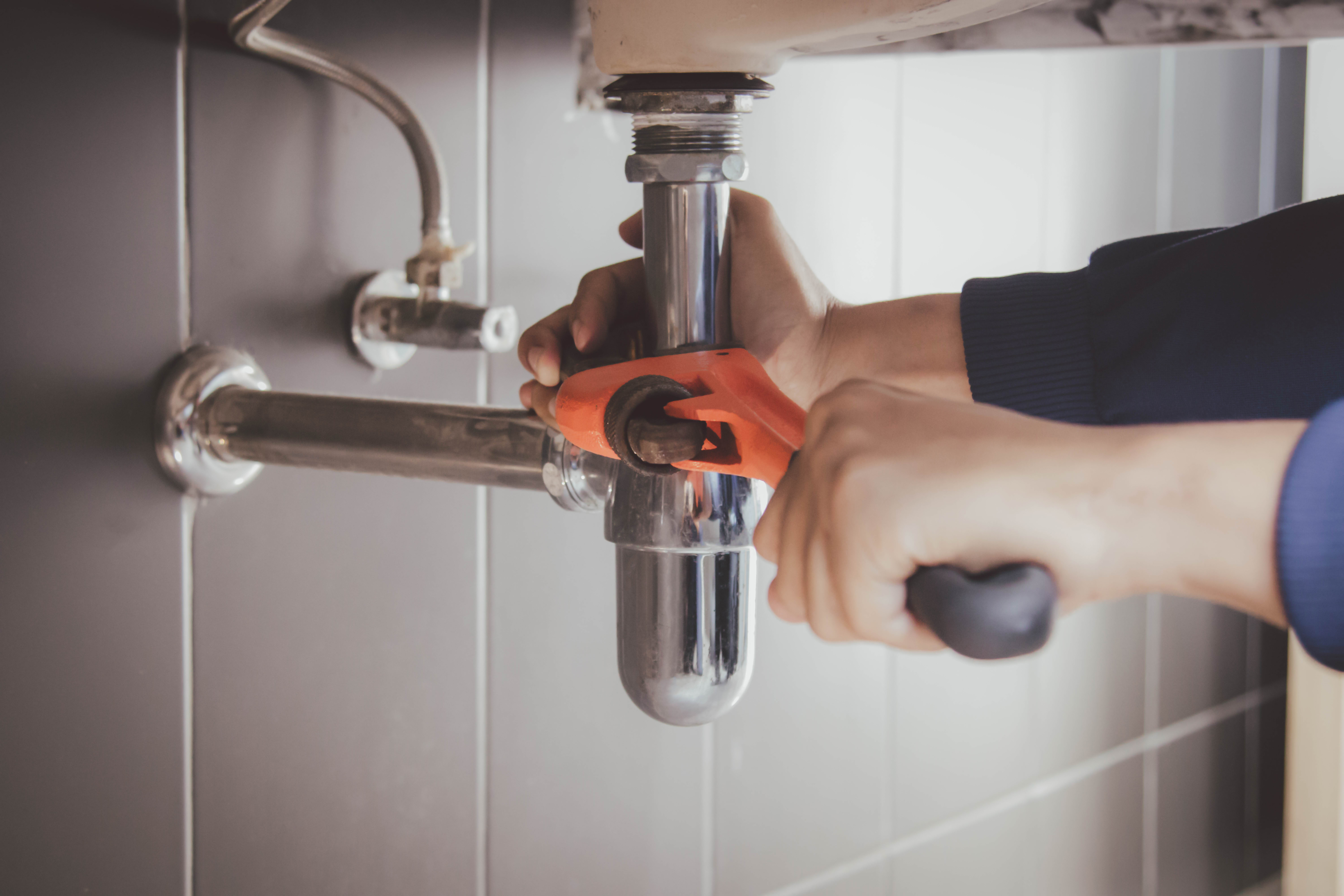 An image of a WyattWorks Plumbing service provider working on pipes under a bathroom sink.