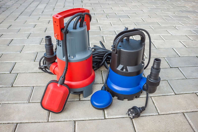 An image of two sump pumps sitting on a driveway - call WyattWorks for sump pump and sewer services in Huntersville, NC.